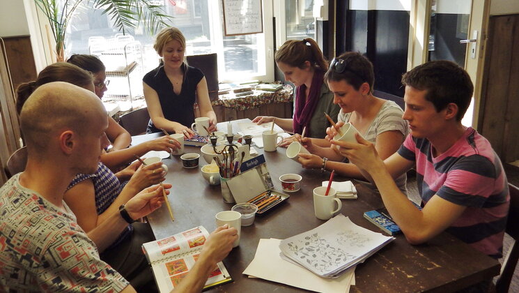 Students in ceramics class sitting around a table painting