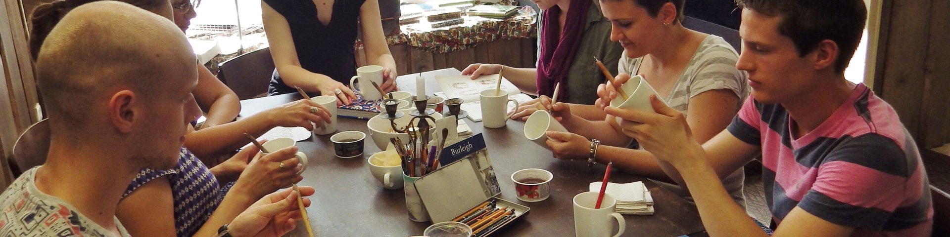 Students in ceramics class sitting around a table painting